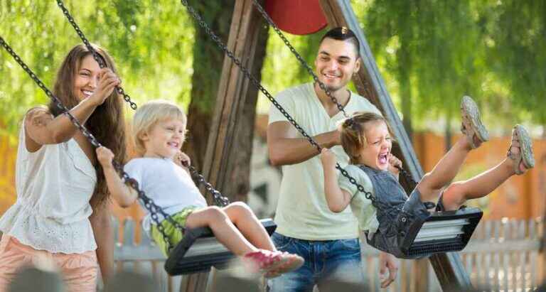 happy young family of four at playgrounds swings