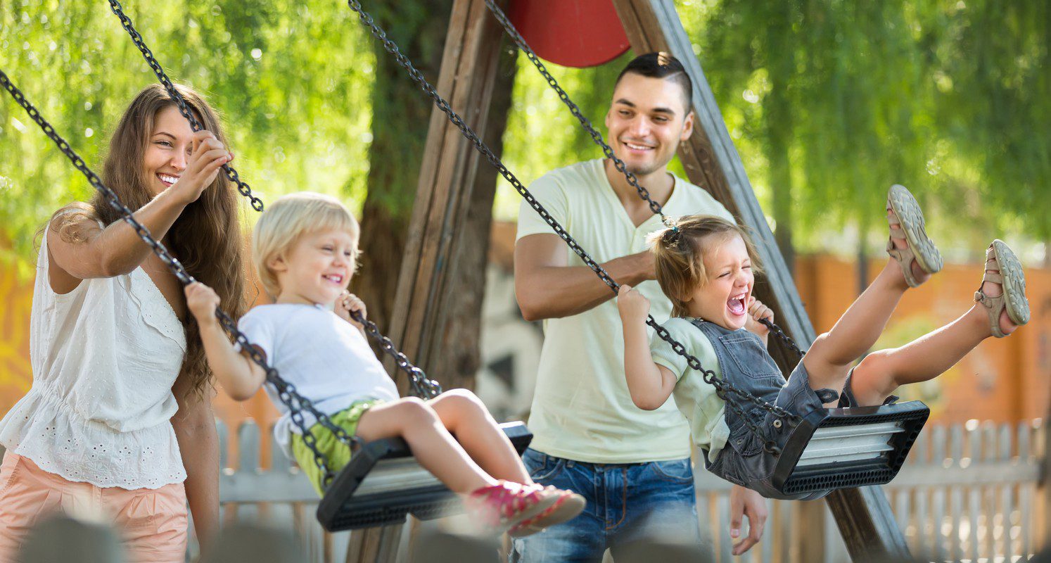 happy young family of four at playgrounds swings