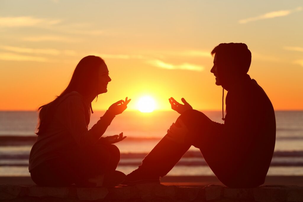 couple sitting on the beach with the sun in the middle