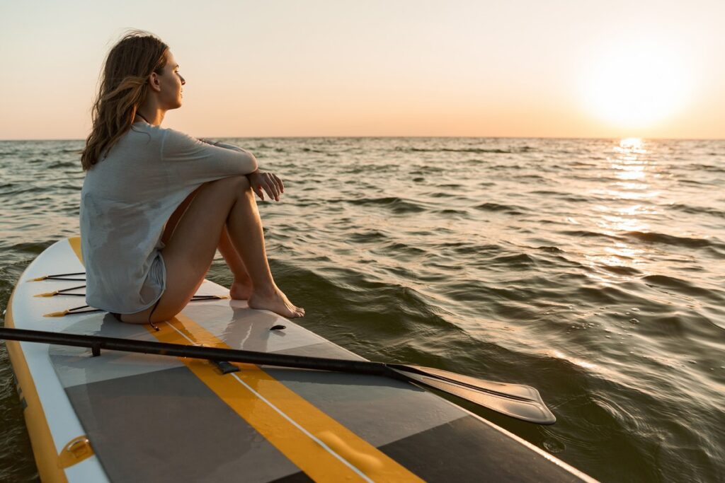 beautiful young woman sitting on a stand up paddle board on a water