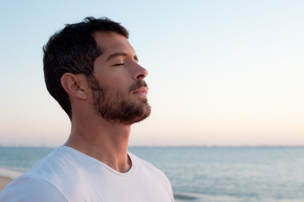 handsome man wearing white deep breathing in front of the ocean