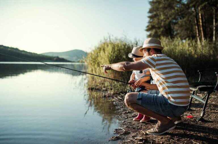 A mature father with a small son outdoors fishing by a lake