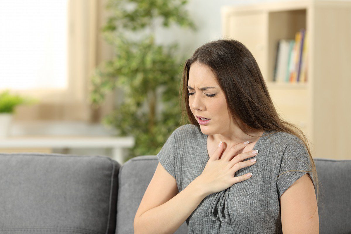Woman suffering respiration problems sitting on a couch in the living room